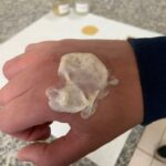 Formulação cosmética com partículas naturais de bocaiúva aplicada sobre o dorso de uma mão.