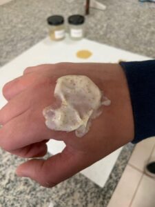 Formulação cosmética com partículas naturais de bocaiúva aplicada sobre o dorso de uma mão.