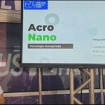 Integrante do projeto AcroNano apresenta a proposta diante de tela com o nome e a equipe do projeto.