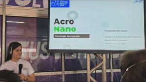 Integrante do projeto AcroNano apresenta a proposta diante de tela com o nome e a equipe do projeto.