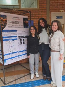 Pesquisadoras diante do pôster sobre o mecanismo de ação antimicrobiana do peptídeo D-18.