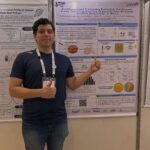 Antolin Júnior diante do pôster sobre creme cosmético contendo compostos bioativos da bocaiuva.